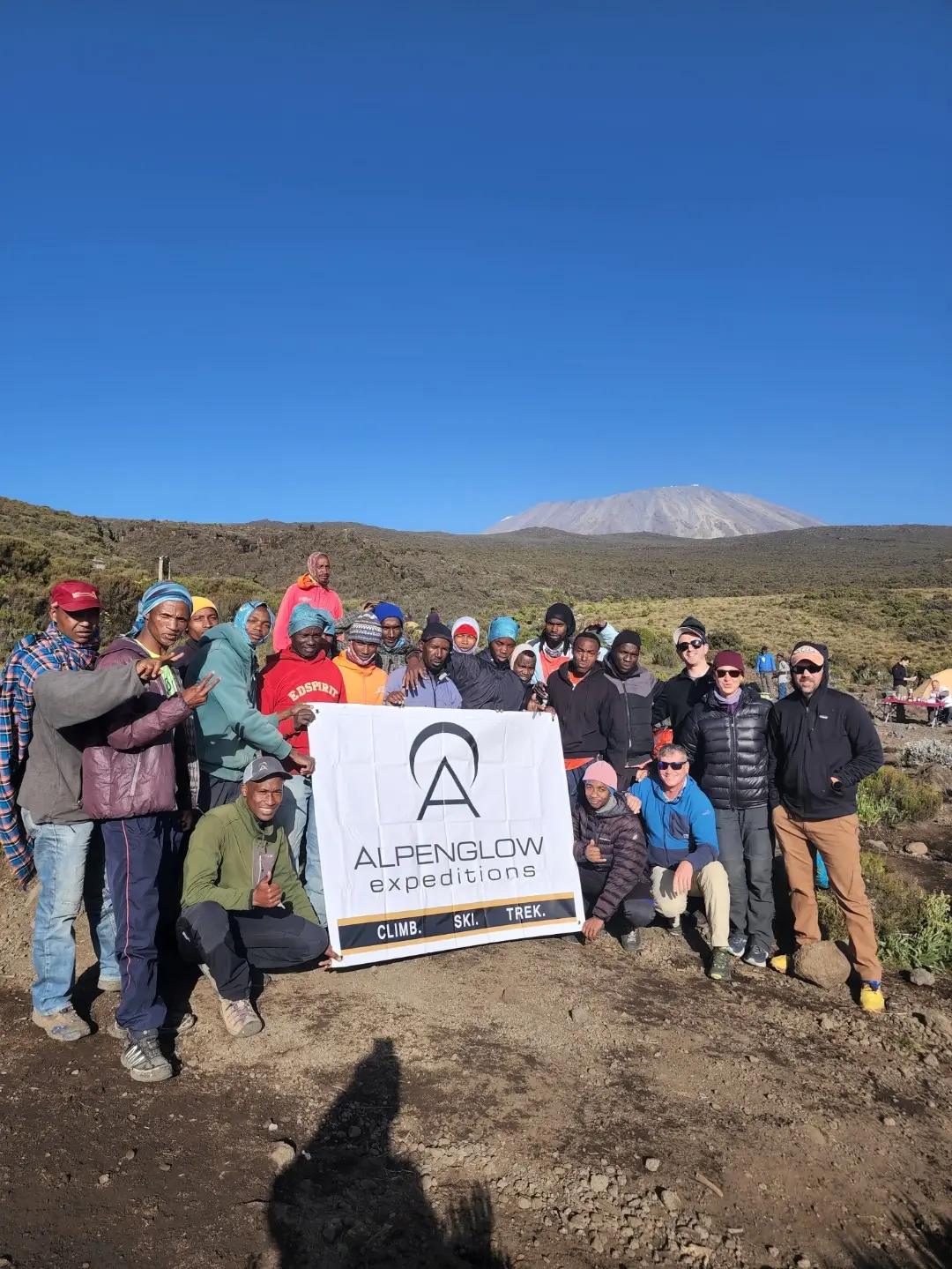 Kilimanjaro Expedition clients posing with an Alpenglow Expeditions sign