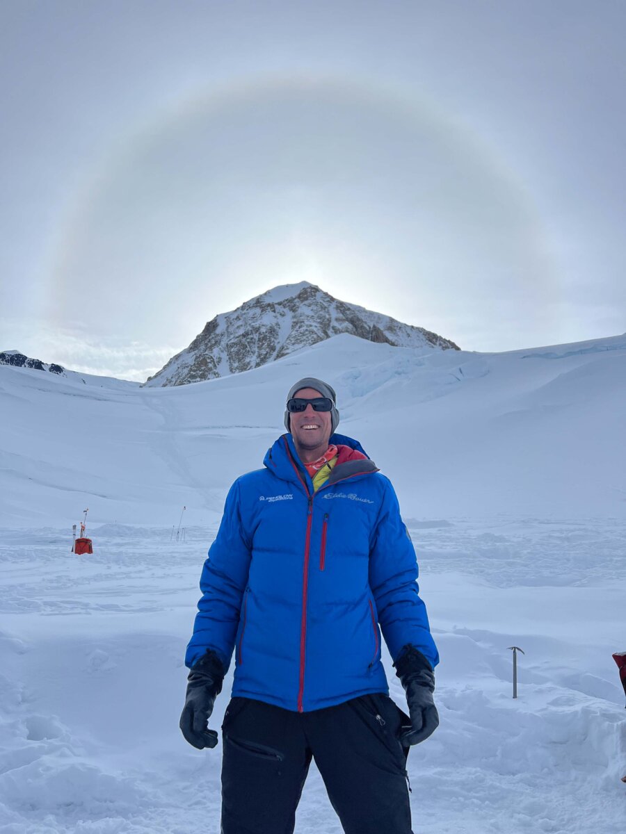 Guide Mike Pond standing in front of the summit of Denali with a sun dog around the summit of Denali.