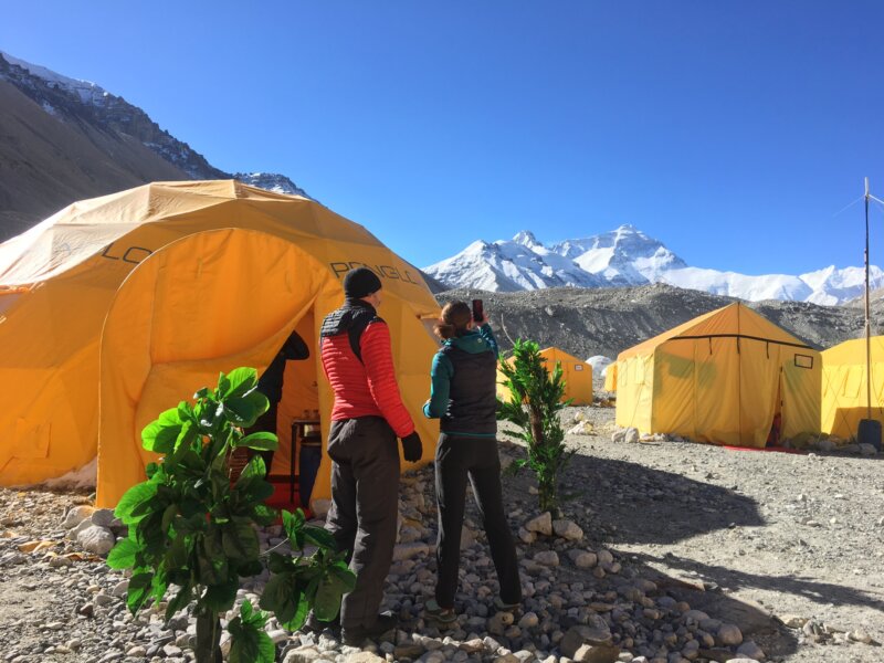 Two hikers standing in front of a yellow expedition tent at Everest Base Camp with a view of Everest in the background