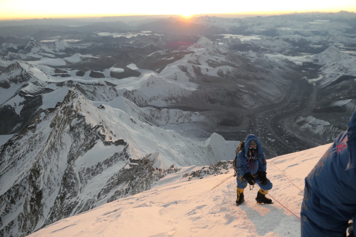 A sherpa team member of Alpenglow Expeditions climbs near the summit of Mt Everest with the sunrising in the background above snow capped peaks. 