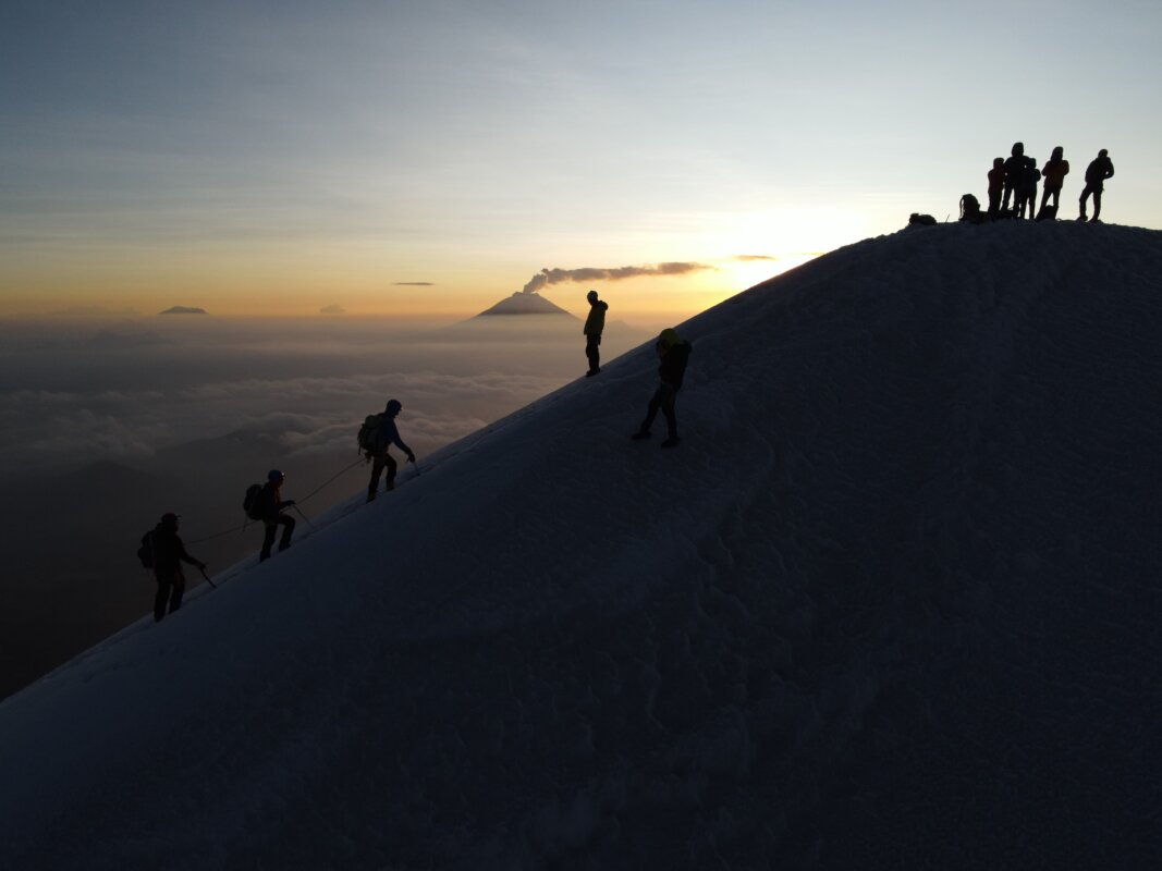 Beginner mountaineering students on an intro to high-altitude mountaineering course in Ecuador, taught by Alpenglow Expeditions' professional mountain guides, climbing to the summit of a volcano at sunrise.