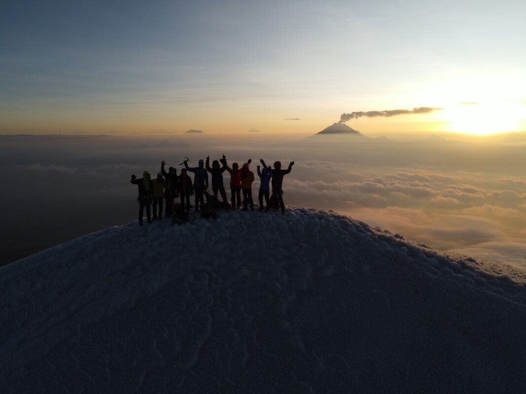 Beginner mountaineering students on an intro to high-altitude mountaineering course in Ecuador, taught by Alpenglow Expeditions' professional mountain guides, standing on a volcano at sunrise.