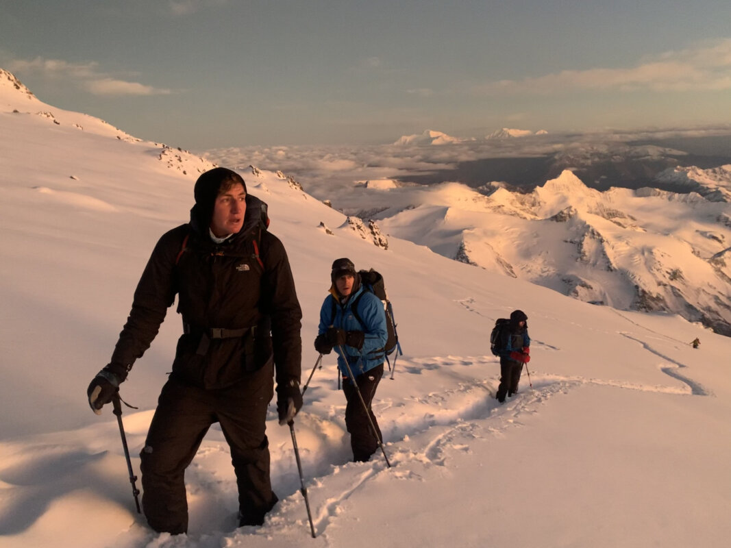 Three climbers ascend a snowfield at sunrise on Aconcagua.