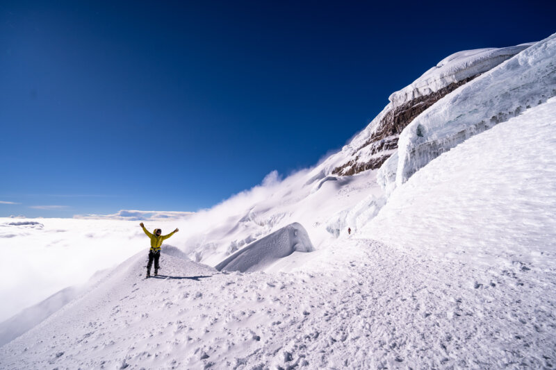 Mountaineer raising their arms in achievement while climbing Cotopaxi on Alpenglow Expeditions' Cotopaxi Rapid Ascent Expedition.