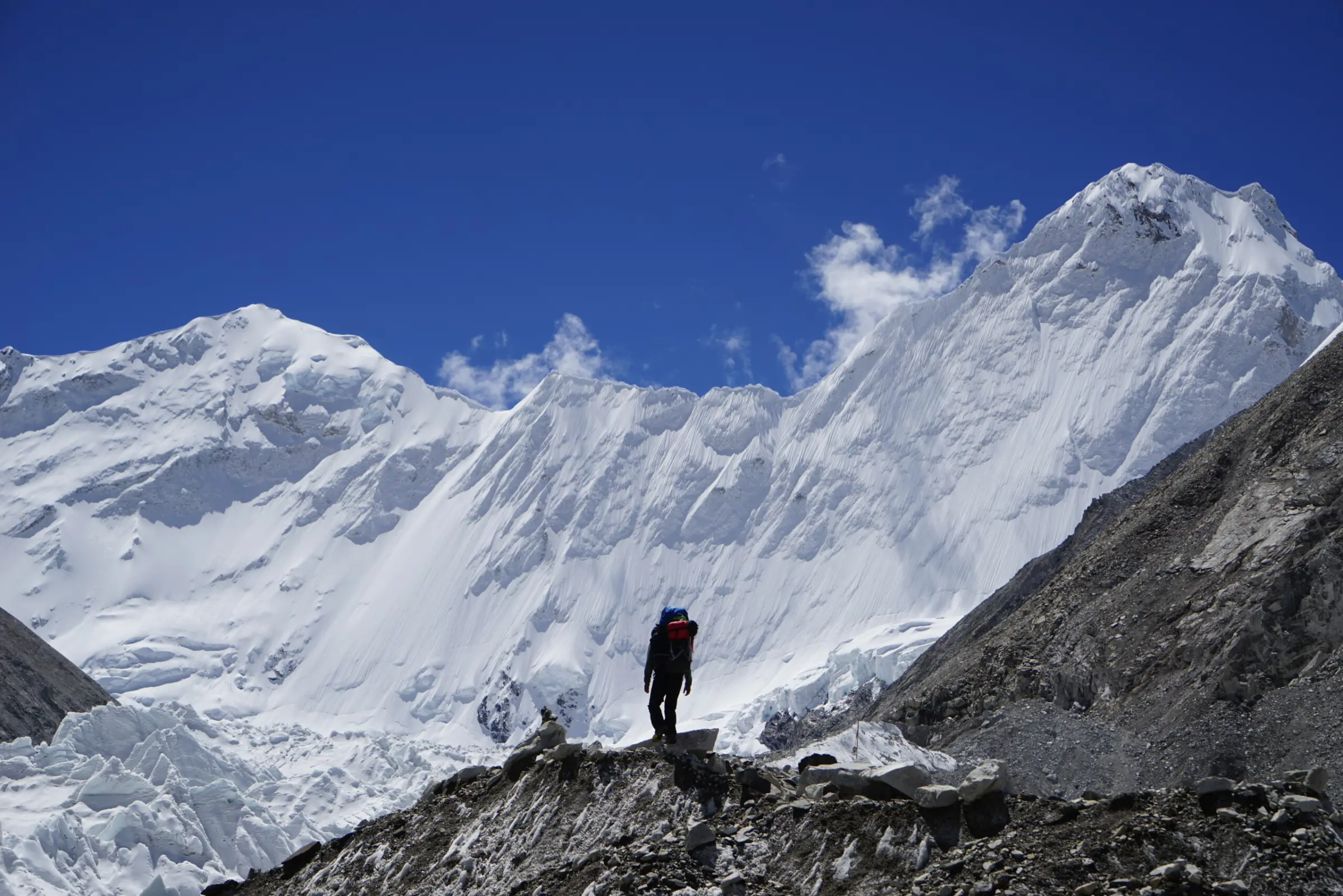 Person standing in front of Cho Oyu during an expedition, with a beautiful white mountain background and clear blue skies during a guided expedition with Alpenglow Expeditions..