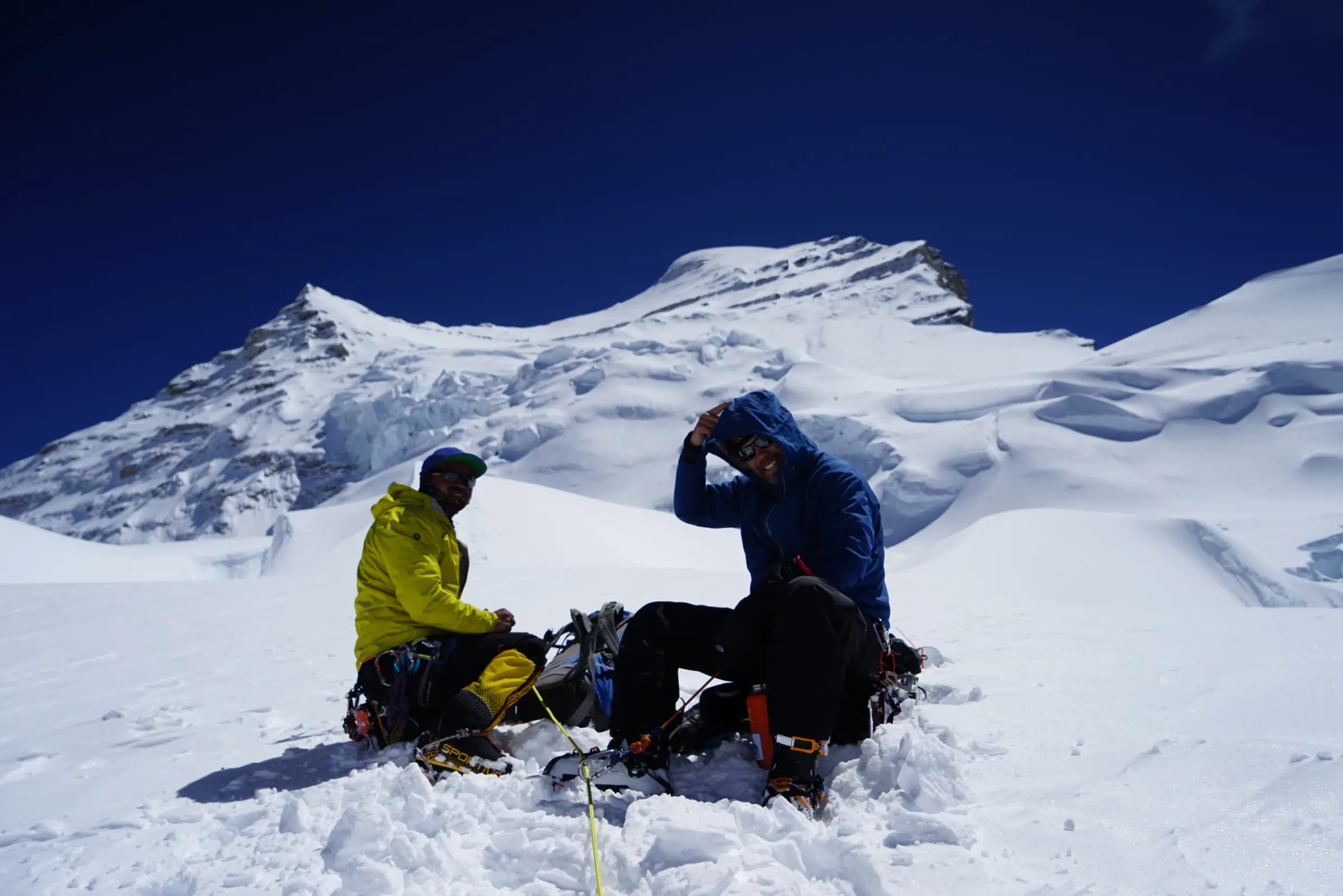 Two climbers sitting eating lunch on a snowy slope during a Cho Oyu Expedition with Alpenglow Expeditions.