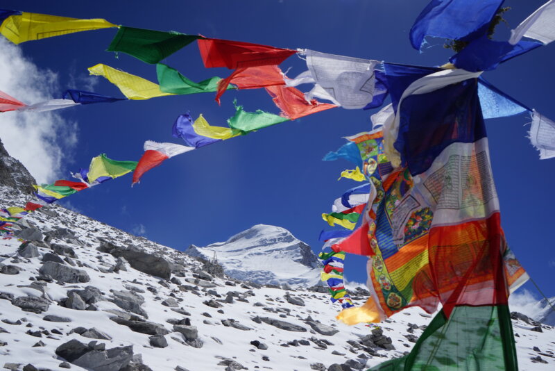Prayer flags on a Cho Oyu Expedition with tents in the background during a guided expedition with Alpenglow Expeditions.
