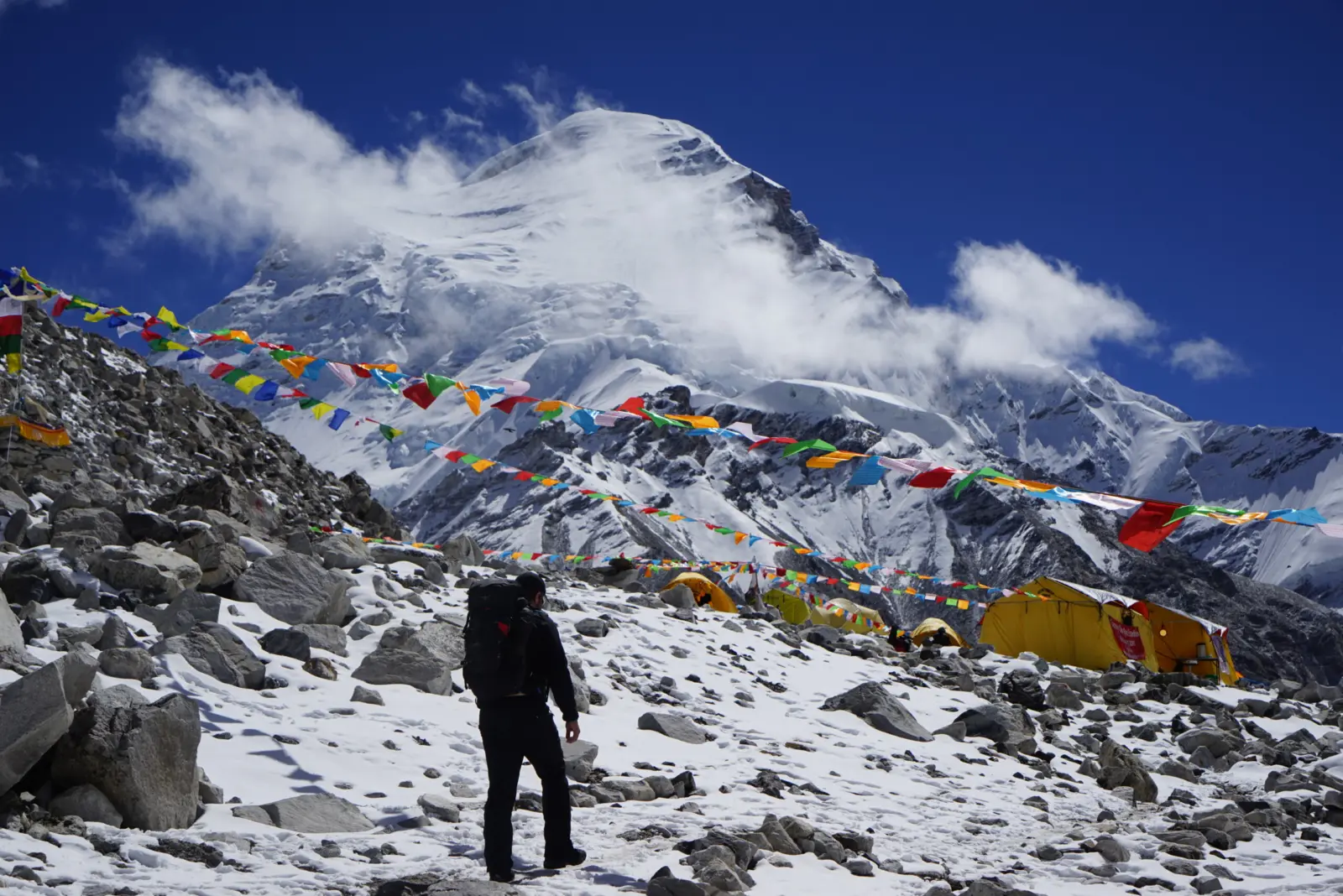 A climber standing in front of tents at a high camp on a Cho Oyu expedition with Alpenglow Expeditions.