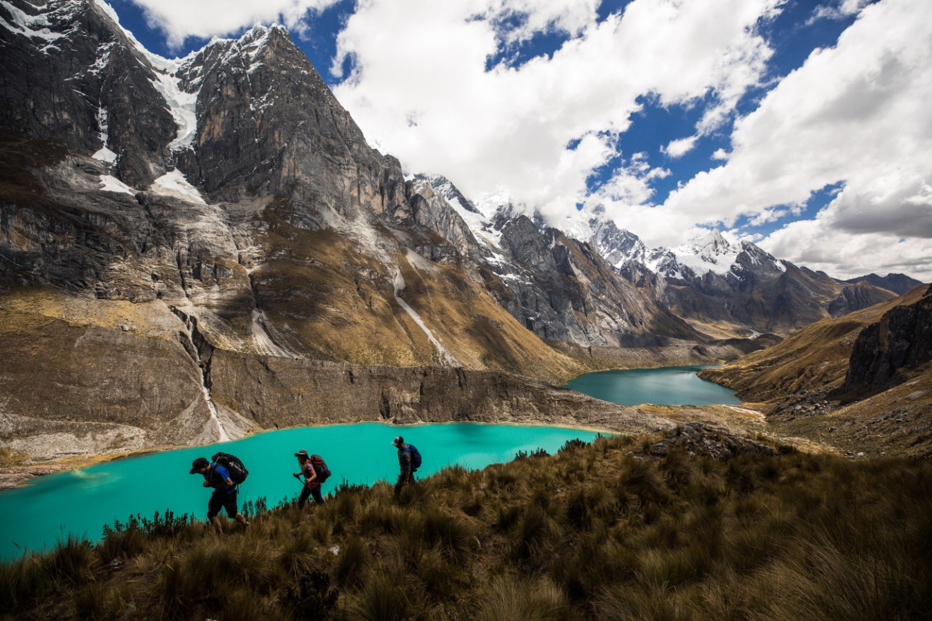 Three hikers on the Cordillera Huayhuash Trek in front of a green lake.