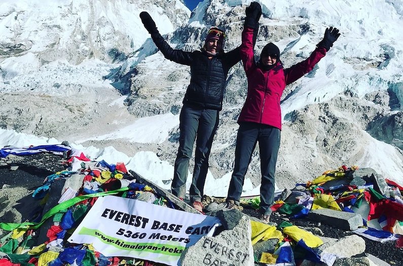 Two hikers raising their arms in triumph upon arriving at Everest Base Camp.