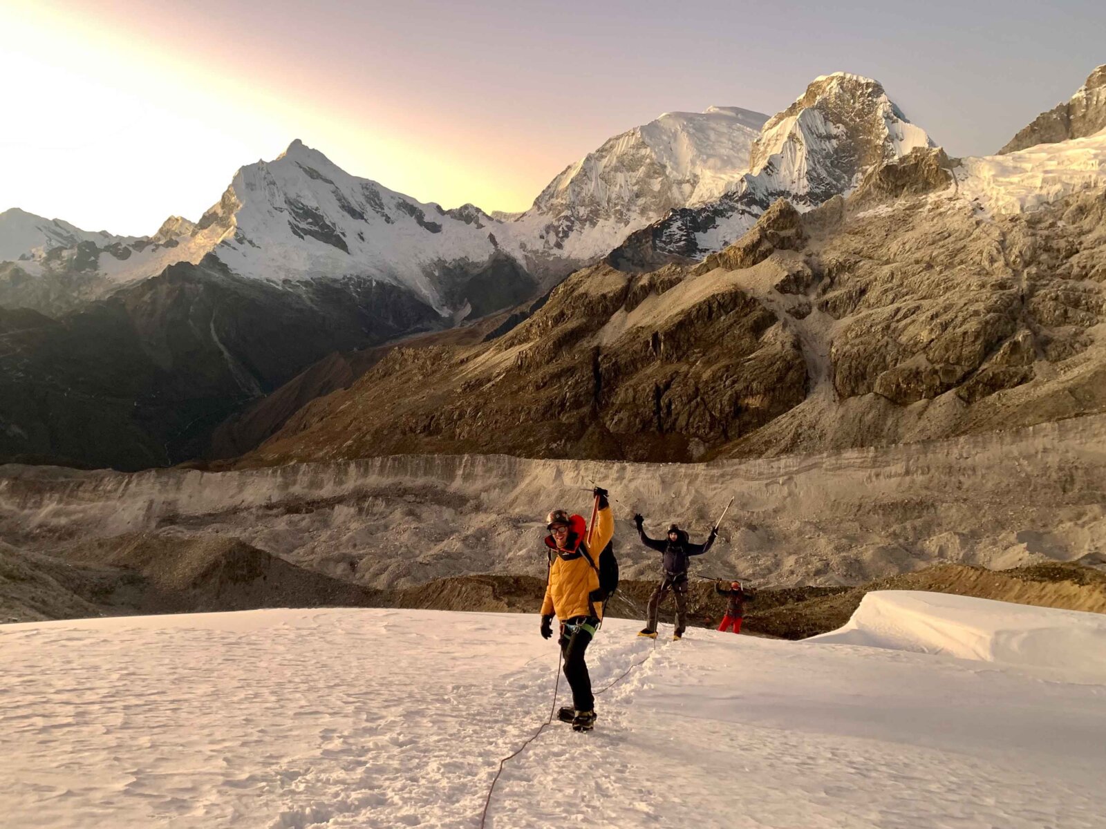 Two mountaineering raising their arms in triumph while standing on a glacier at sunrise in Peru.
