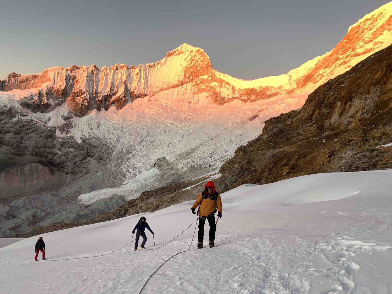 Climbers ascending a glacier on a peak in Peru at sunrise.