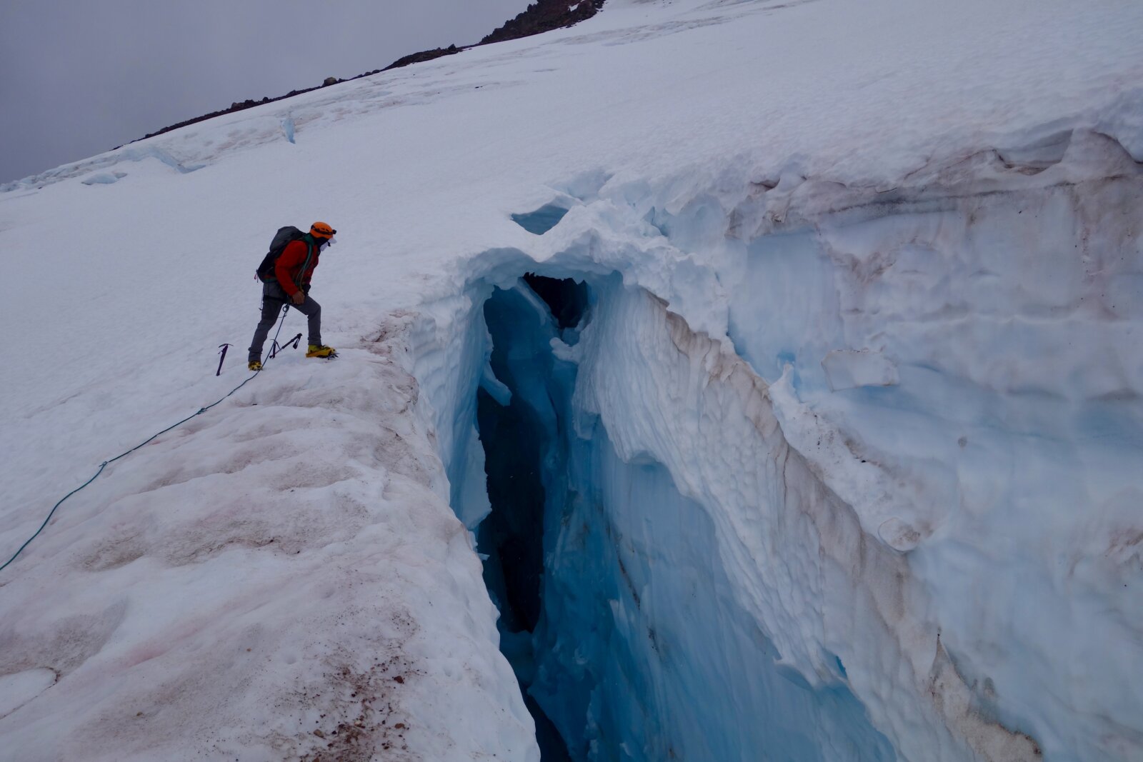 Mountaineer peering into a crevasse on Mount Shasta during an Intro To Mountaineering course with Alpenglow Expeditions