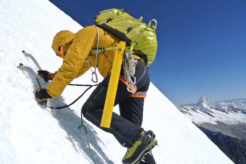 An alpine climber wearing yellow ascending a snowy slope