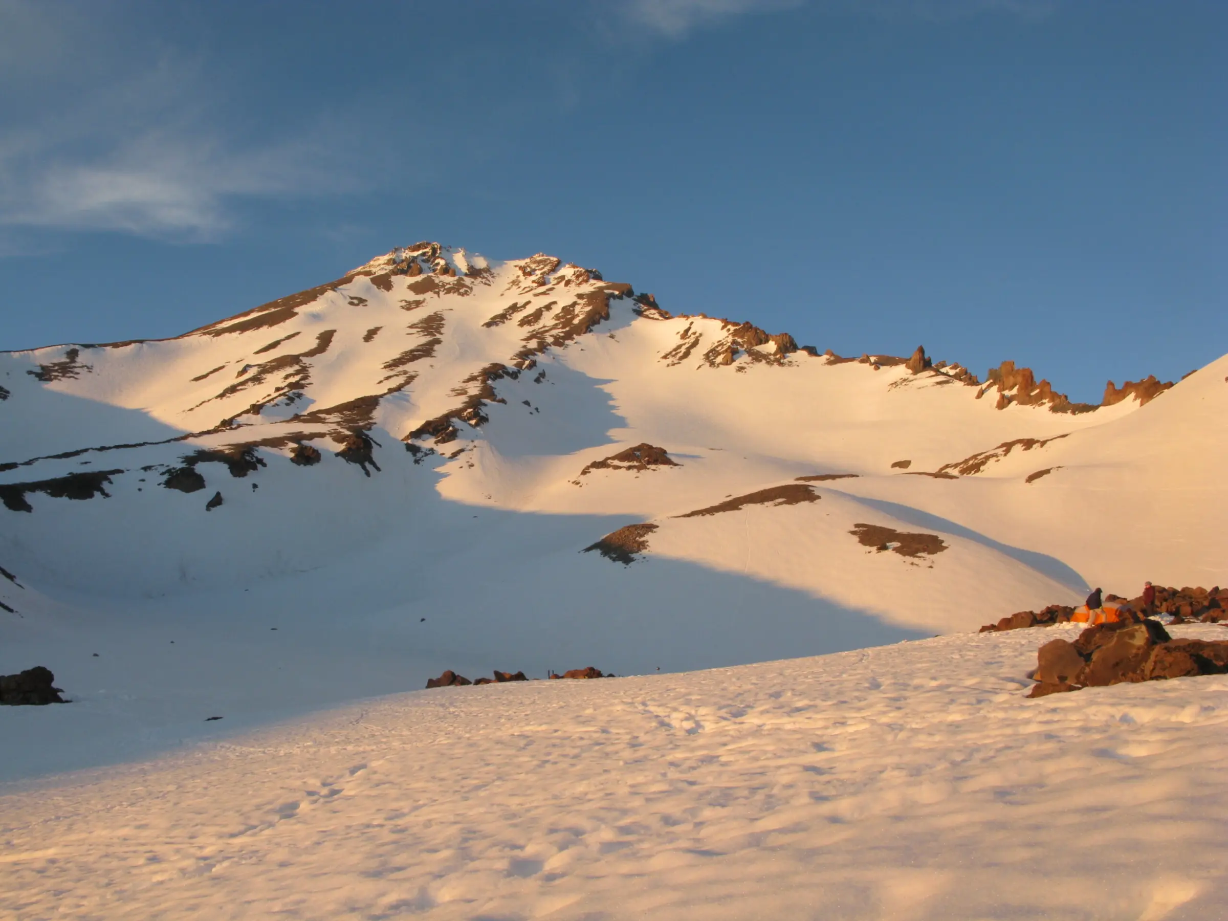 An early morning photo of Mount Shasta covered in snow with a blue sky above during an Alpenglow Expeditions guided trip on Mount Shasta.