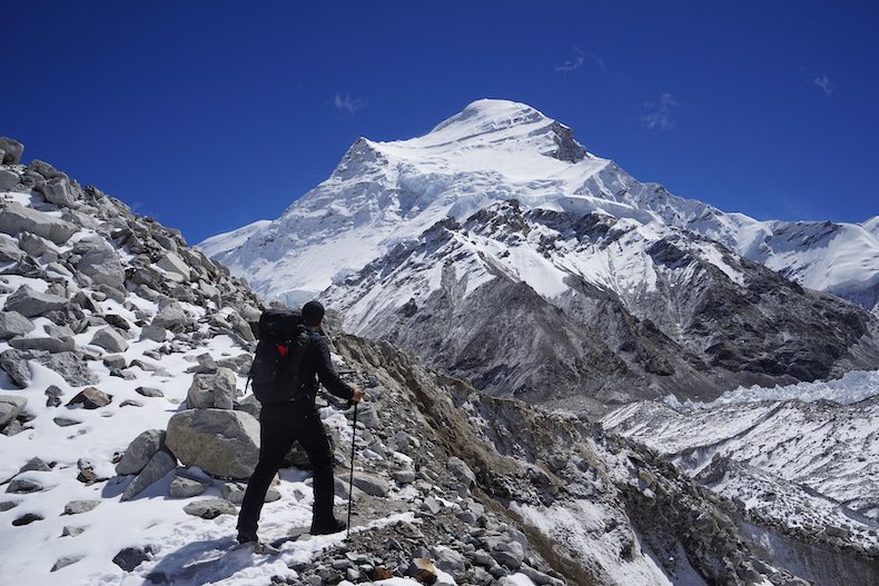 A climber stands with his back facing to the camera with Cho Oyu, the sixth tallest mountain in the world, in the background.