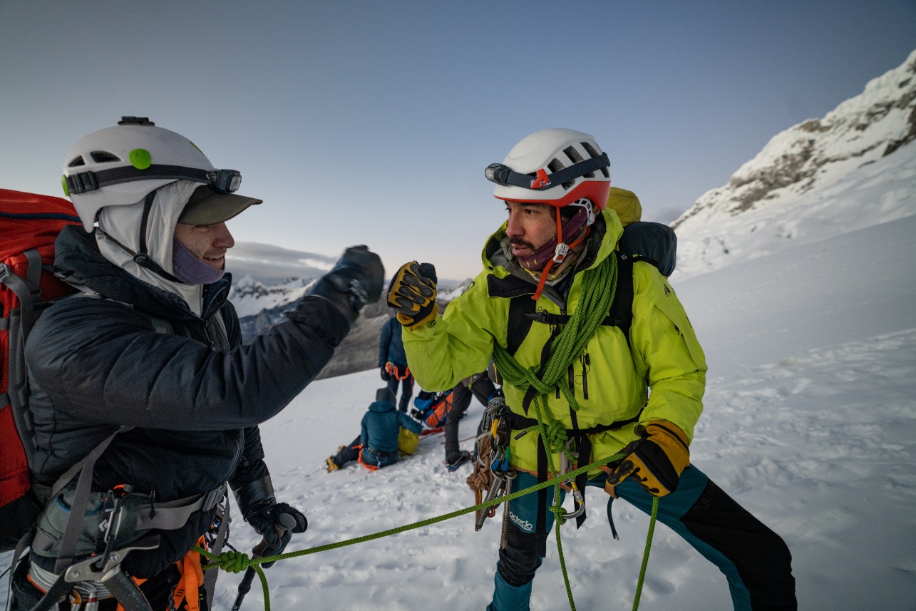 A guide fist bumps a client on the summit of Alpamayo