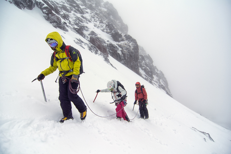 A roped climbing team of three ascends a steep snow field on a volcano in Ecuador.