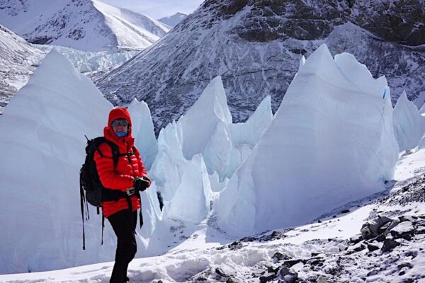 A climber clad in red stands in front of giant white penitentes on the North Side of Mt Everest.