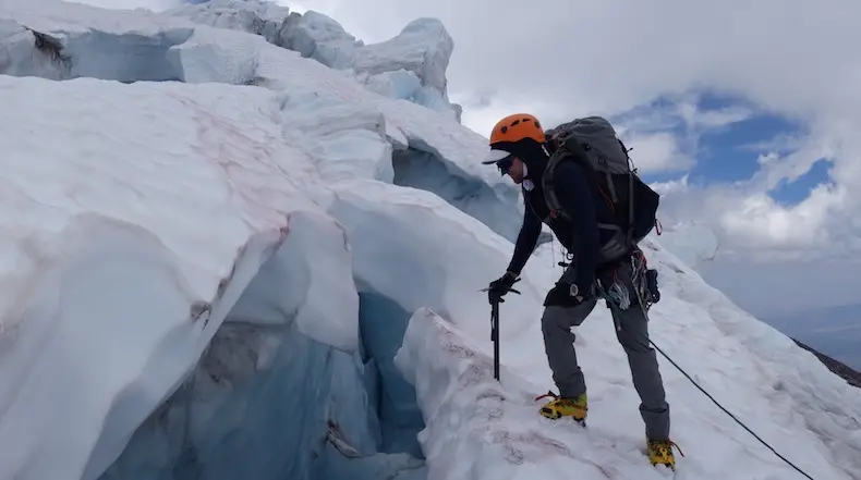 A guide for Alpenglow expeditions leans on his ice ax over the edge of a crevasse on Mt. Shasta.