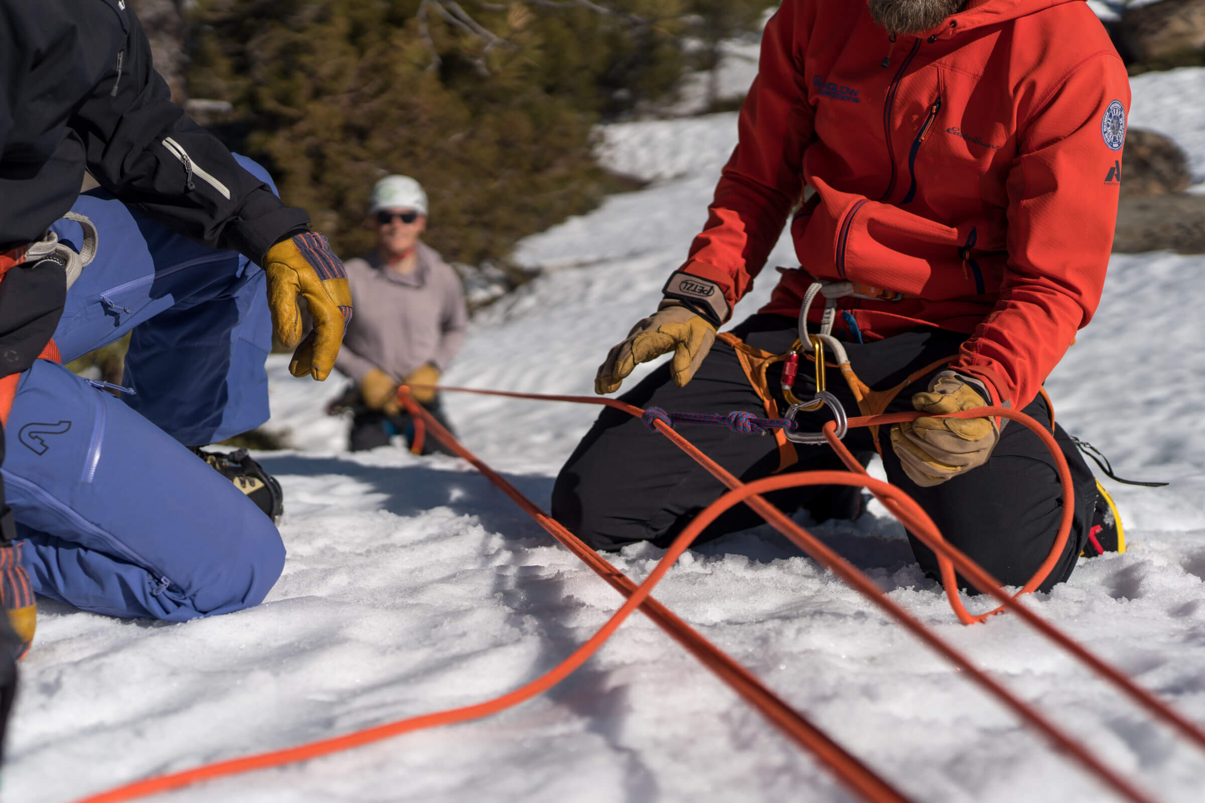 A closeup of a climbing guide from Alpenglow Expeditions holding an orange colored rope in their hands as they explain glacier travel to a nearby student in Lake Tahoe