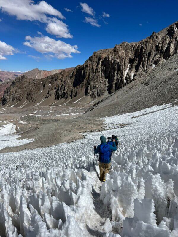 A climber with a blue backpack climbing with Alpenglow Expeditions descends from Camp 1 through tall white snow penitentes on Aconcagua