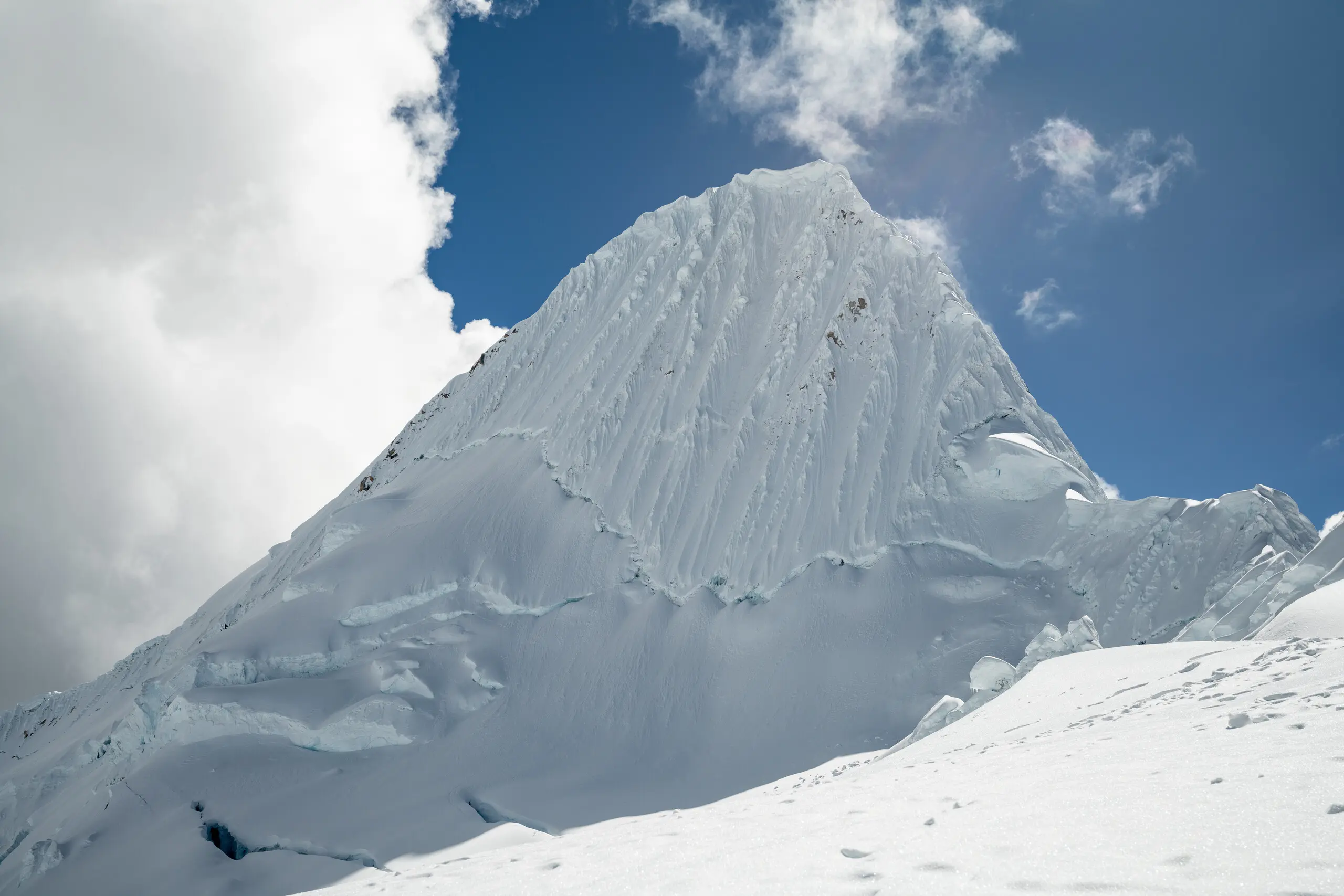 A large white fluted pyramid of a mountain stands before a cloudy blue sky.