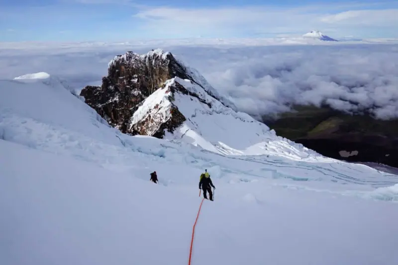 Two climbers scale an expansive white snowfield high above the alpine plains of Ecuador.