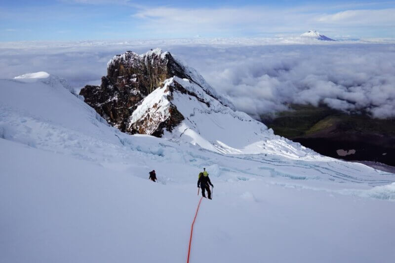Two climbers scale an expansive white snowfield high above the alpine plains of Ecuador.
