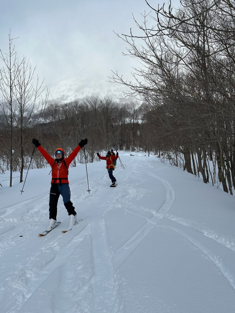 Excited skiers raise their arms in the air while enjoying backcountry skiing in the woods of Japan.