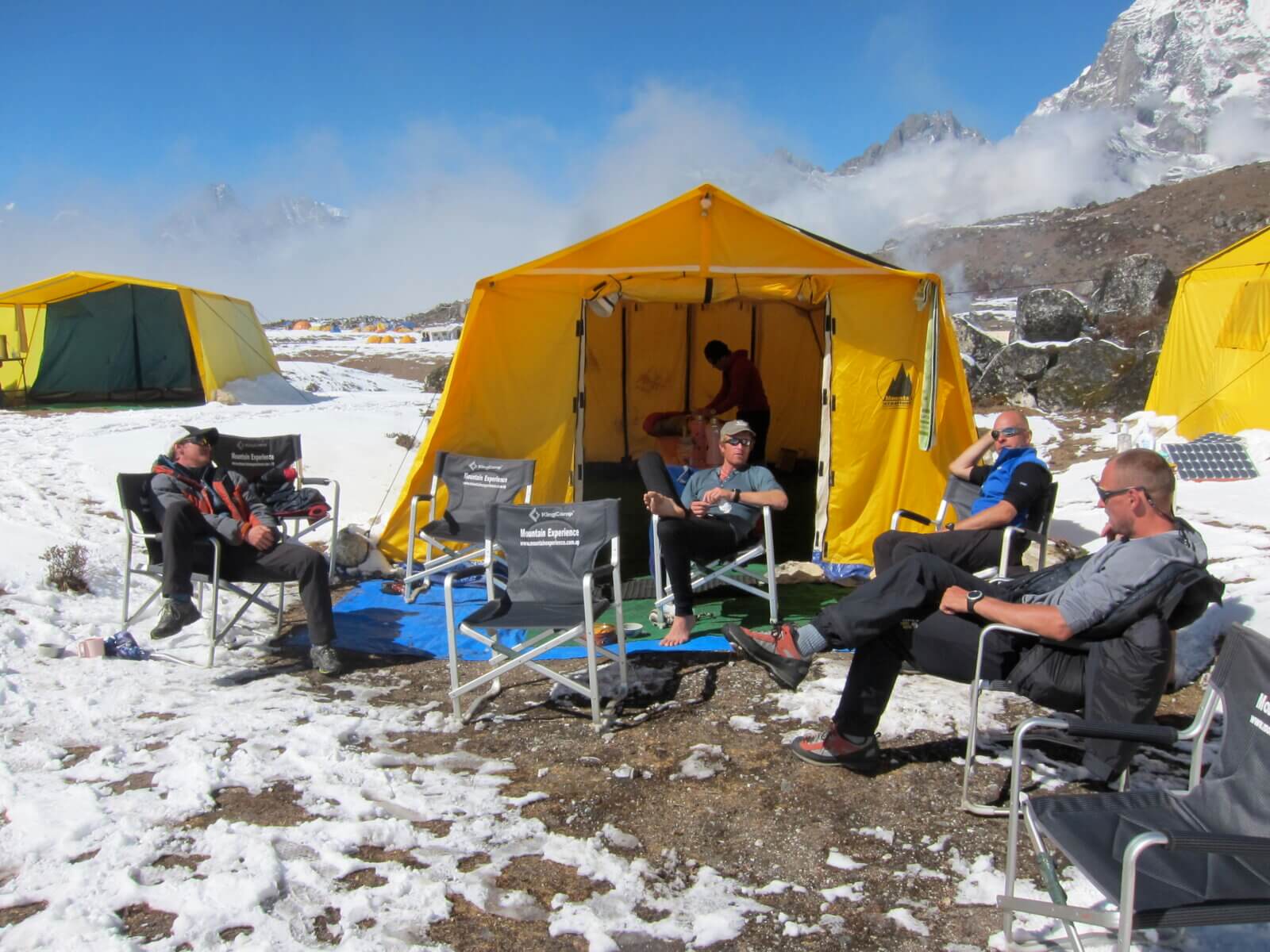 Alpenglow Expeditions team sits outside of a Mountain Experience tent in the Himalaya