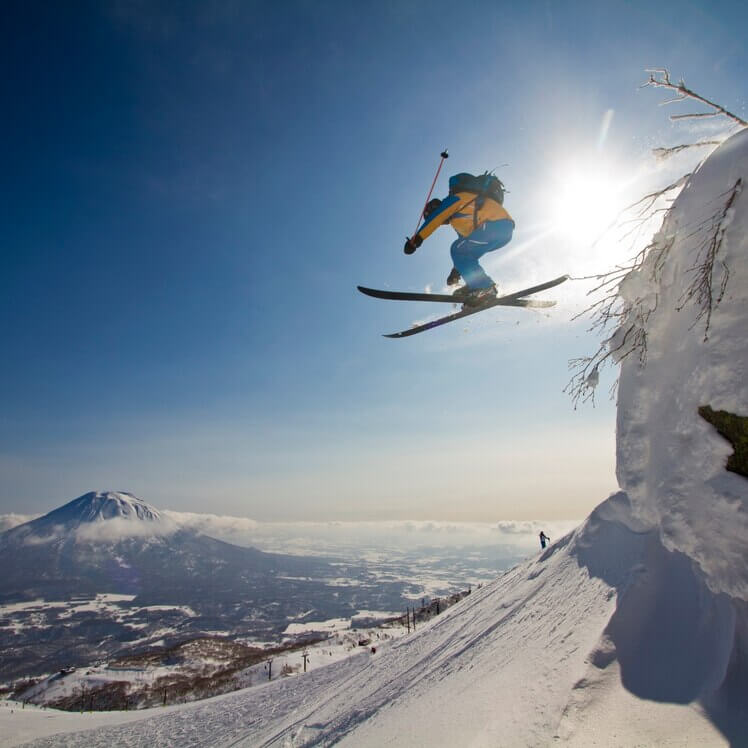 a skier jumps off a small cliff while skiing in Japan