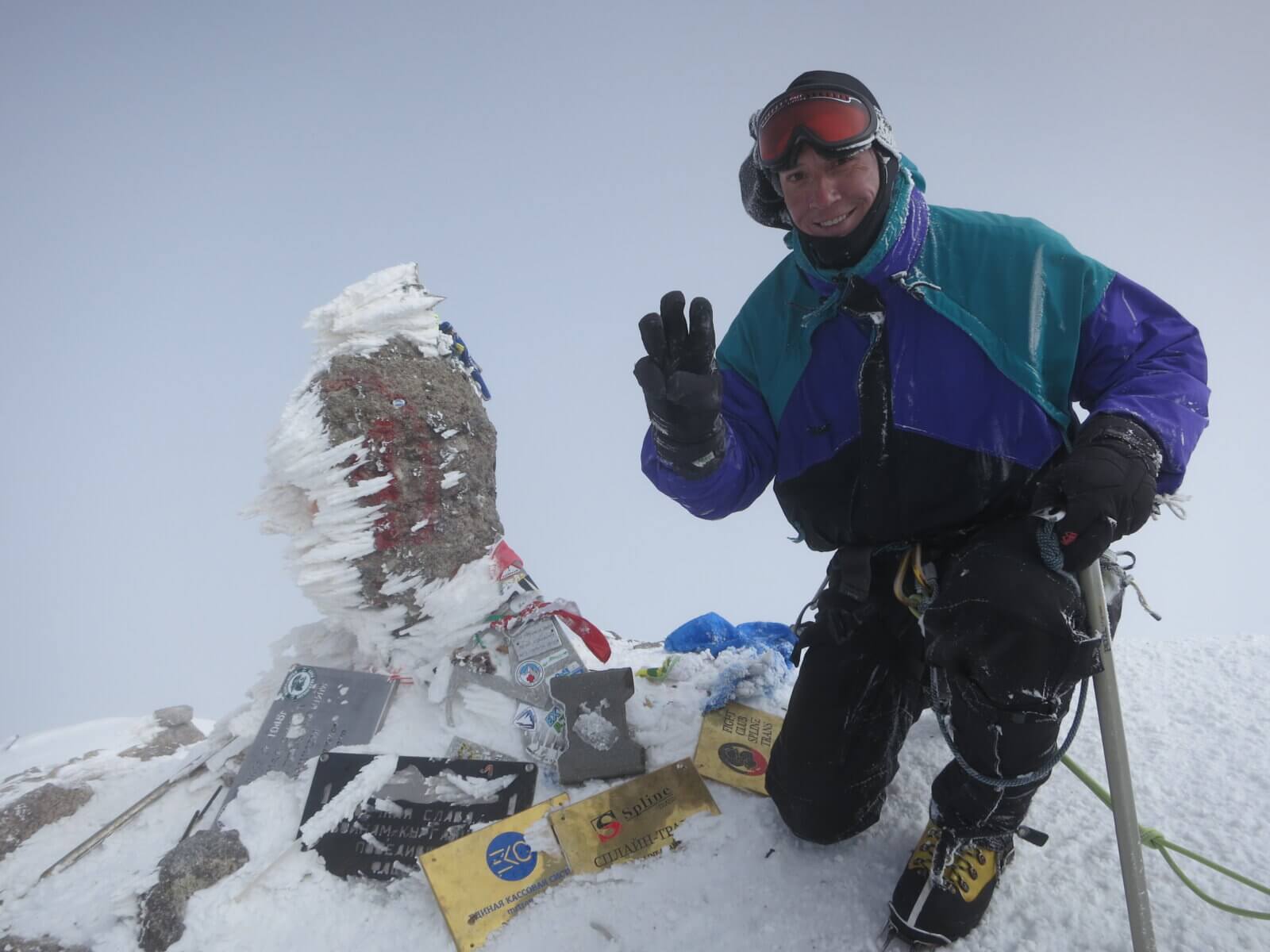 Client kneels next to the summit marker on Peak Lenin during an Alpenglow Expeditions trip.