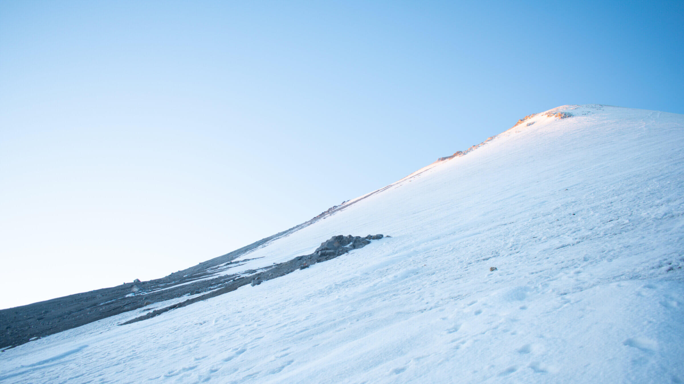 A photo taken from the bottom of the glacier looking toward the summit of Pico de Orizaba beneath a blue morning sky.