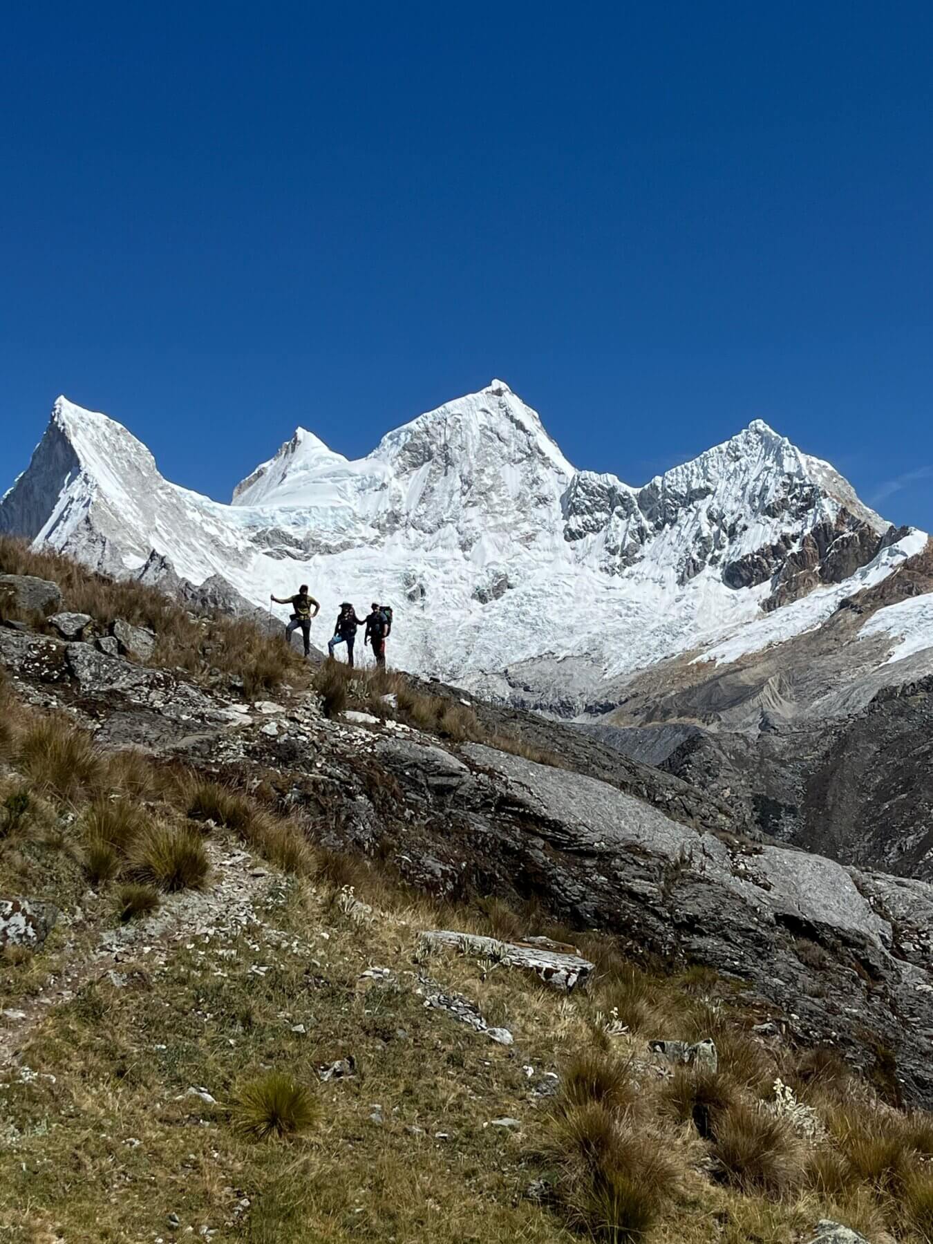 A group of climbers stands in front of 3 snowy peaks in Peru.