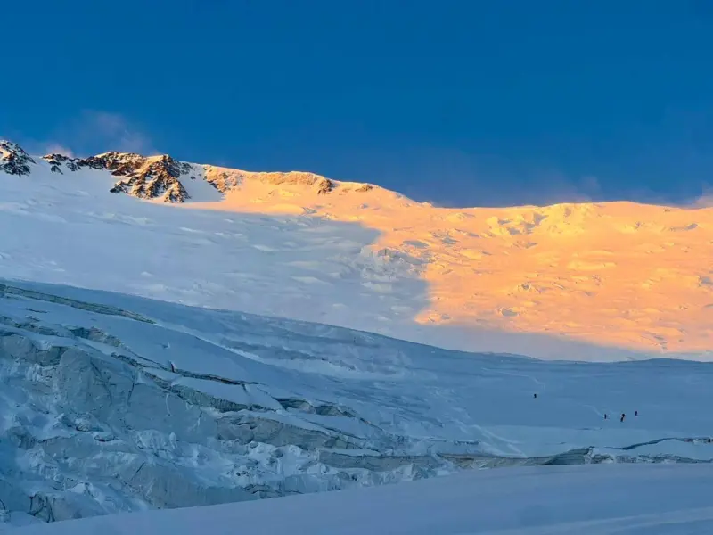 A large white mountain is bathed in golden sunlight under a blue sky.
