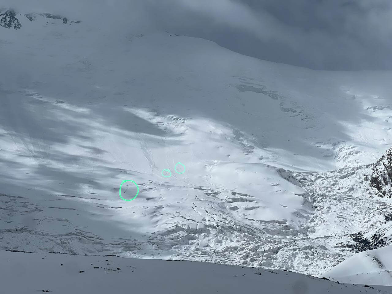 A vast white snowfield with many crevasses, and 3 small circles indicating climbers on the route. 