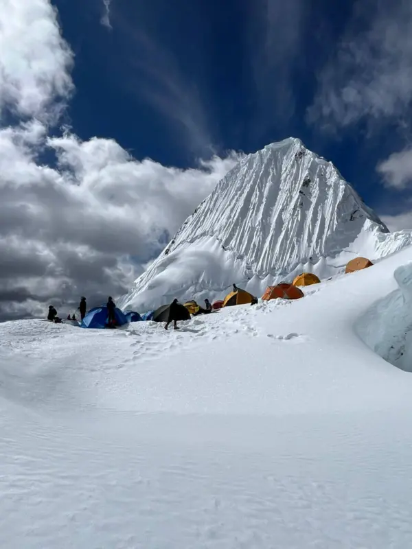 The view of Alpamayo, a large white pyramid of a mountain, from a snow field below.