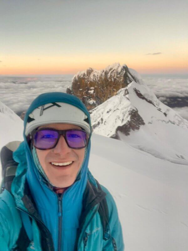 A selfie of a mountain guide on a peak at sunrise.