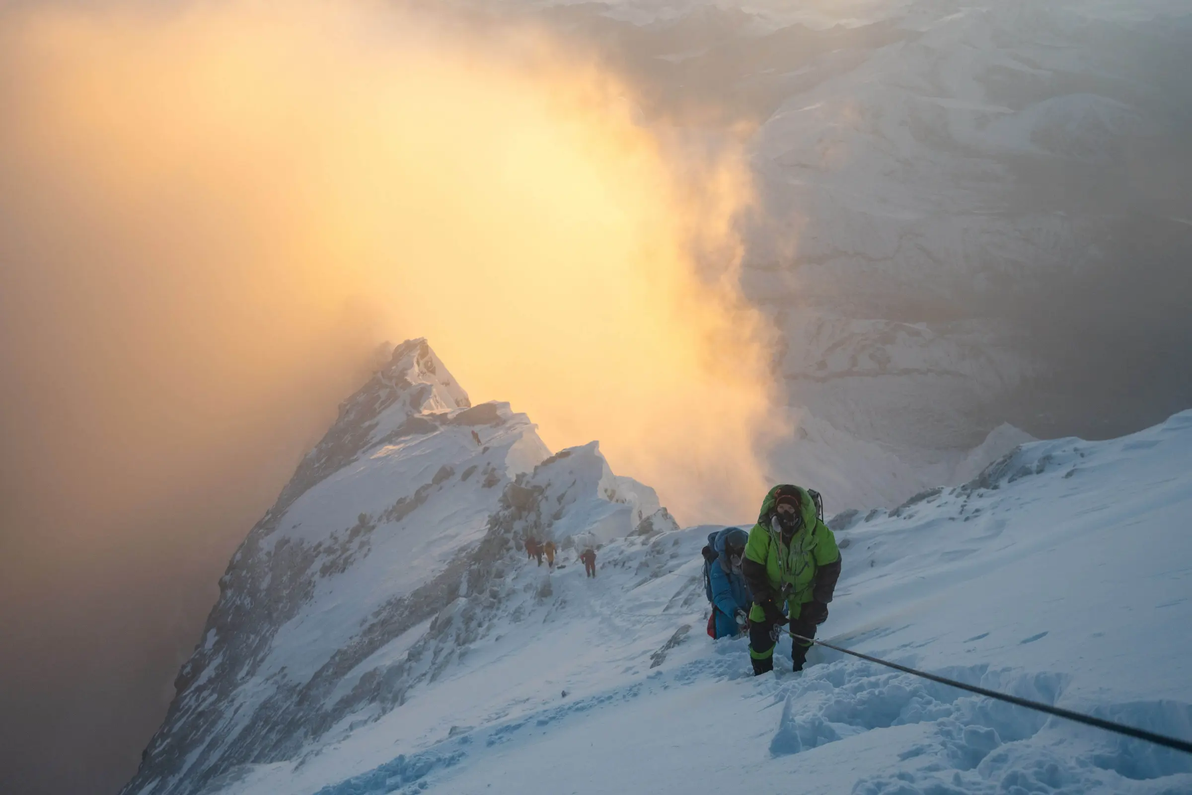Climbers on a snowy slope with a beautiful orange cloud below them.