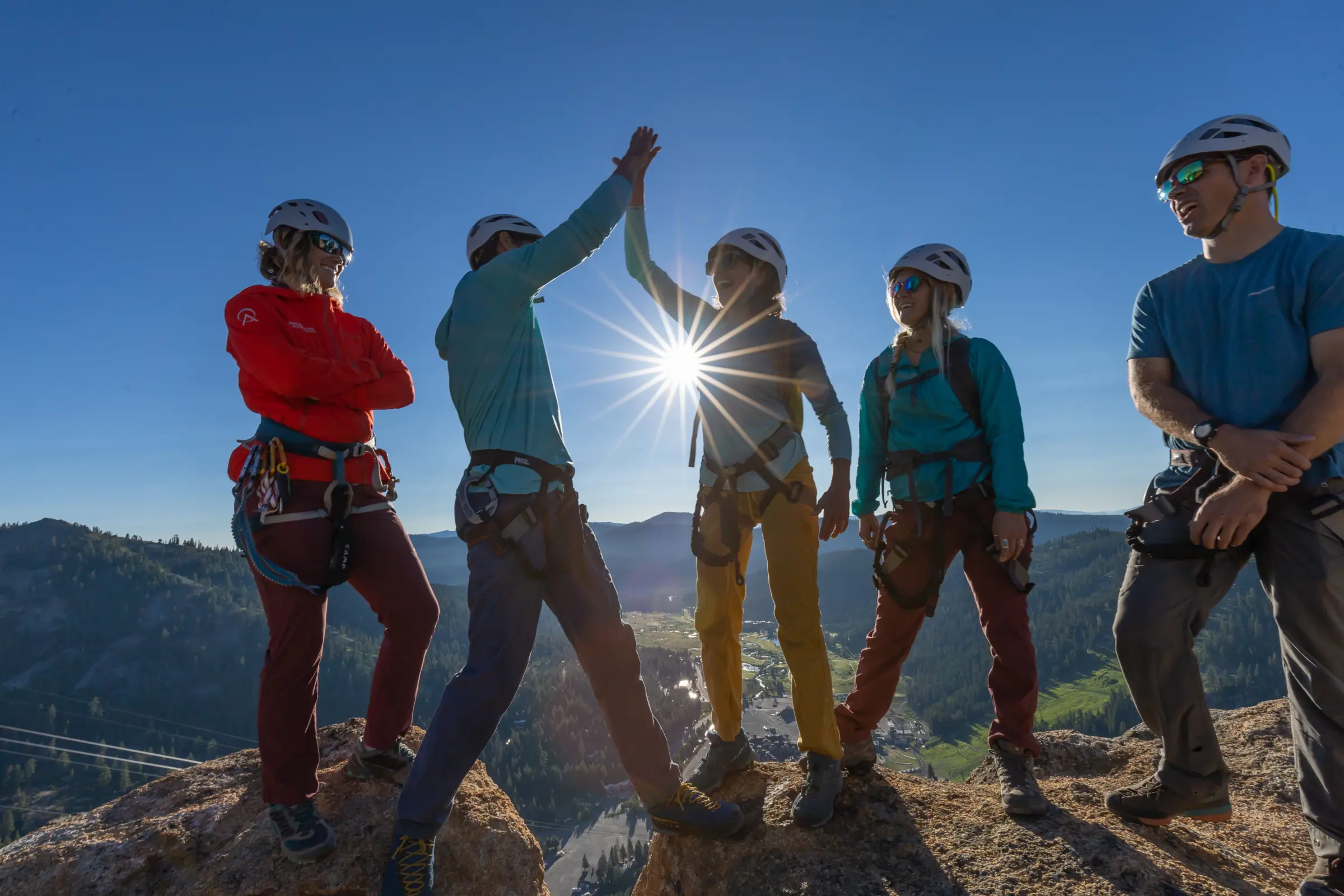A group of 5 climbers with 2 of them high fiving in front of beautiful mountain range and blue sky