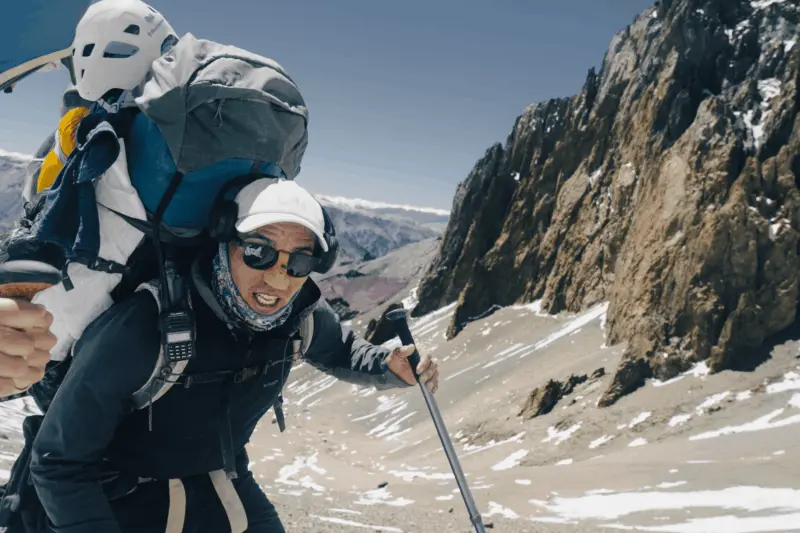A climber resting at high altitude on a snowfield during an Alpenglow Expeditions guided mountaineering expedition